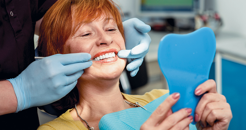 middle aged woman in a dental chair and admiring her new smile in a mirror